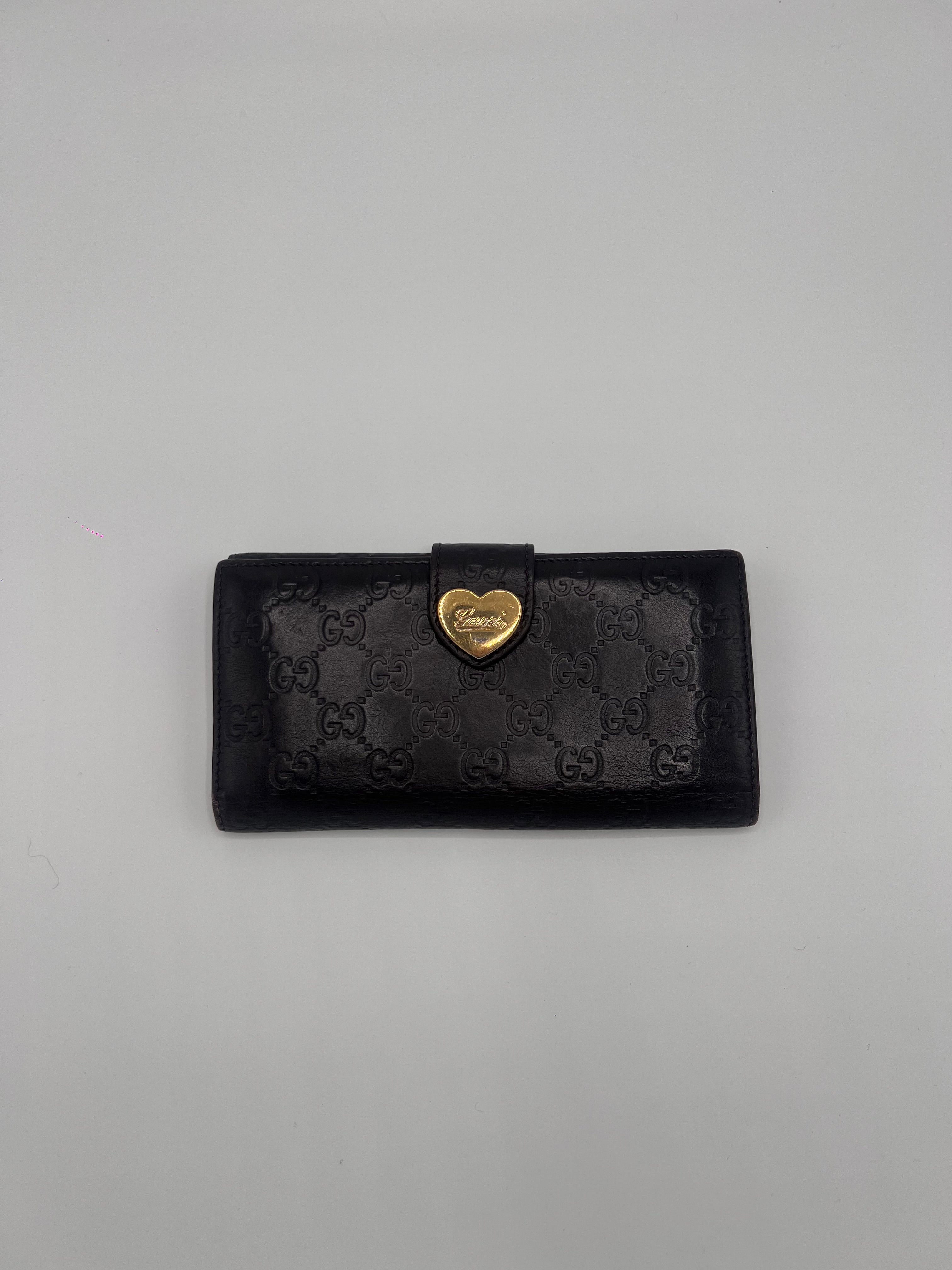 Black/brown Gucci wallet with heart-shaped gold emblem on a gray background